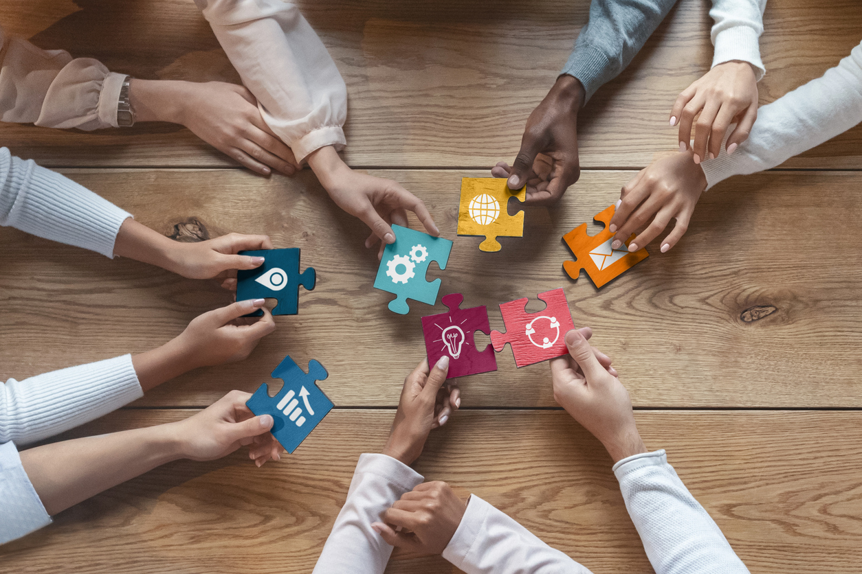 Seven people's hands reaching toward each other with different color puzzle pieces