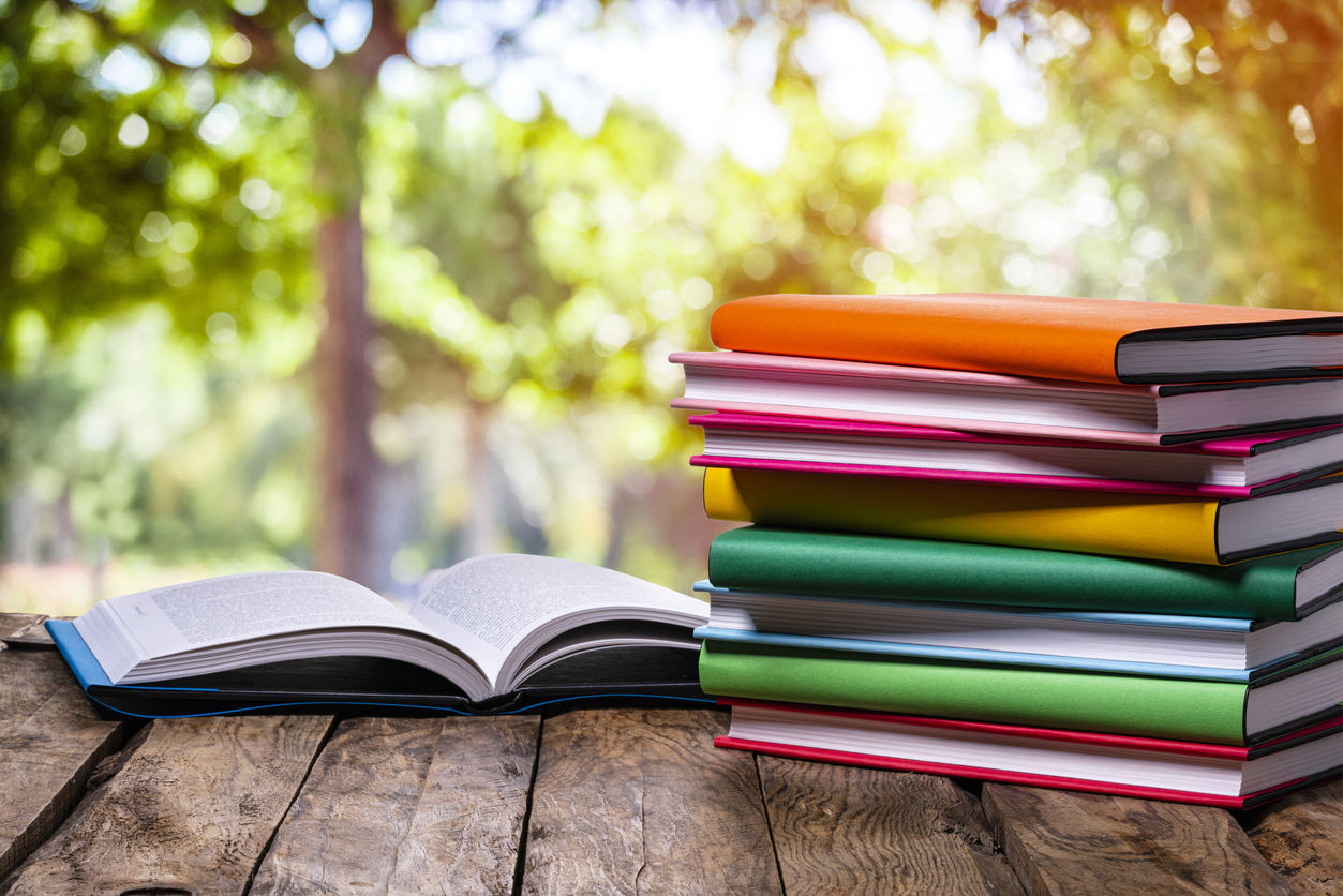 Stack of colorful books on a picnic table in the shade of some trees