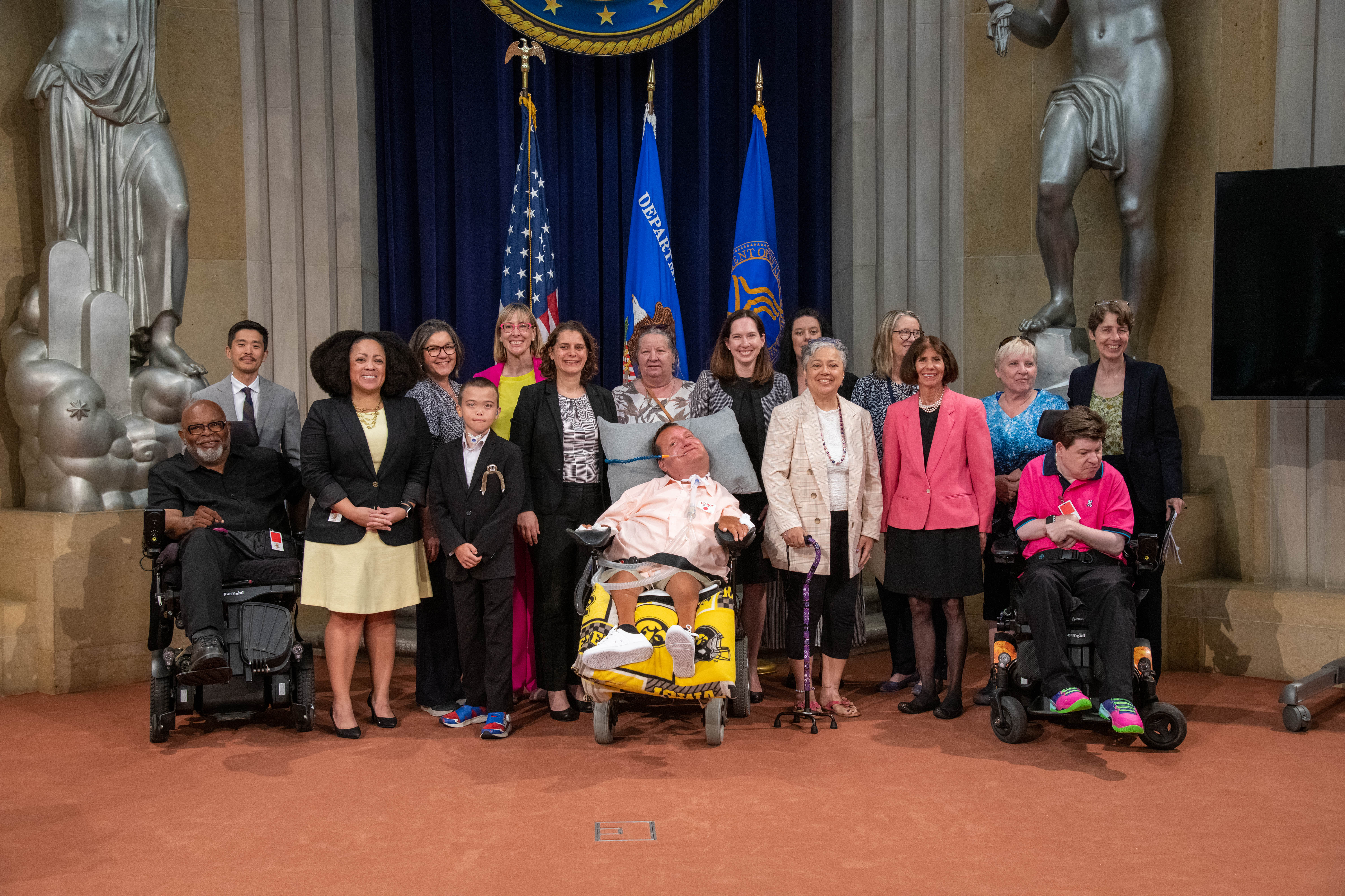 Event panelists and federal officials stand on the stage at the DOJ Great Hall for the 25th Olmstead anniversary event