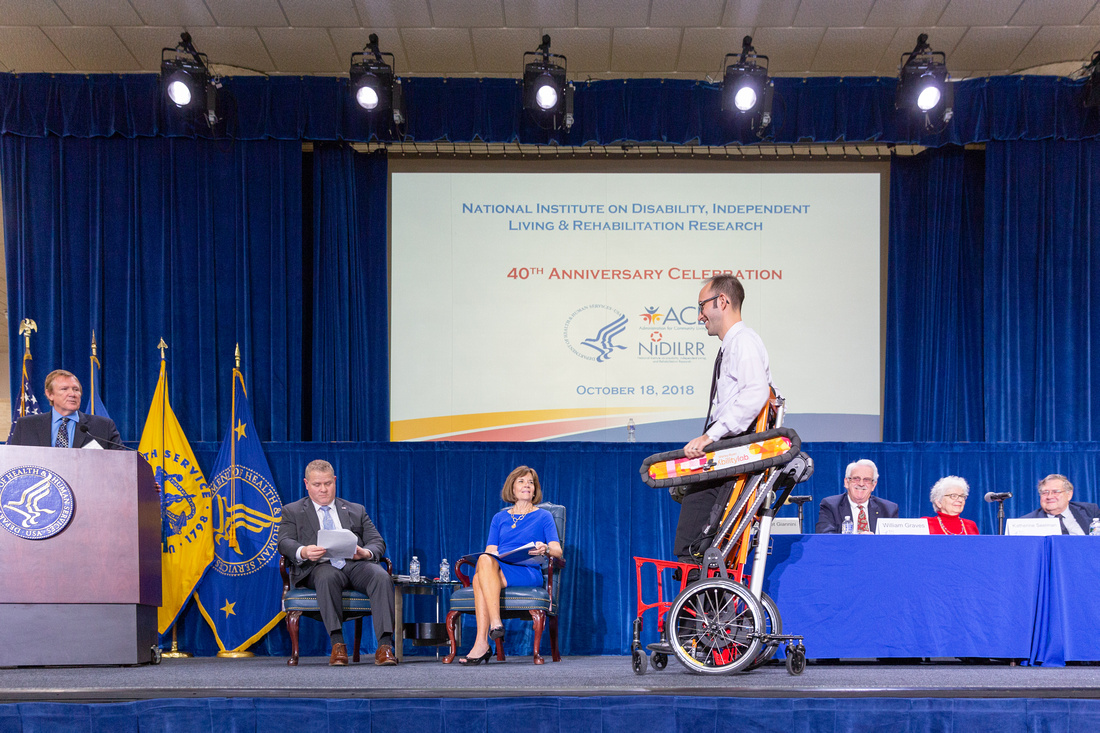 Man strapped into upright wheelchair on stage