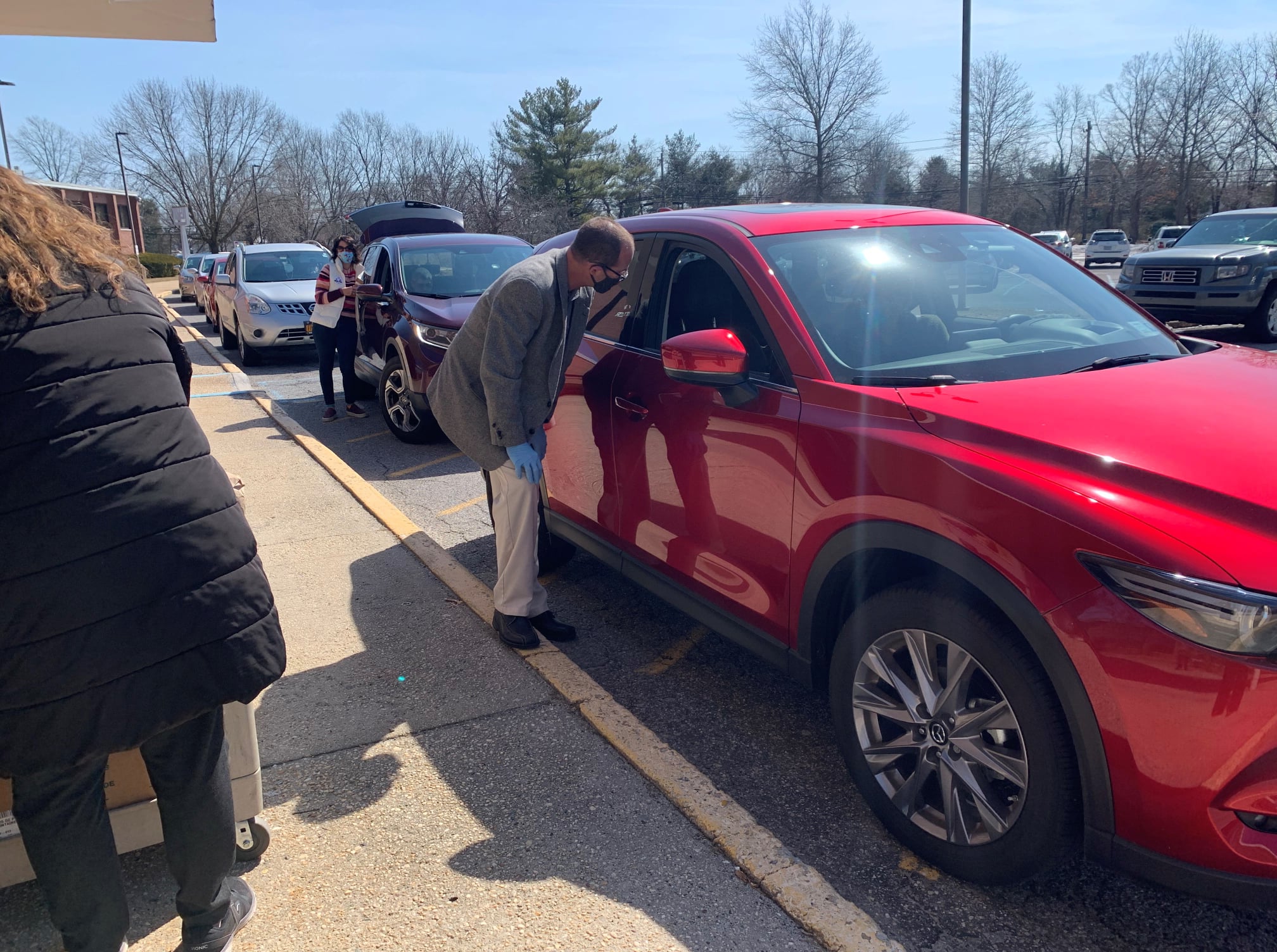 Olsen next to a red car speaking to passengers through an open window