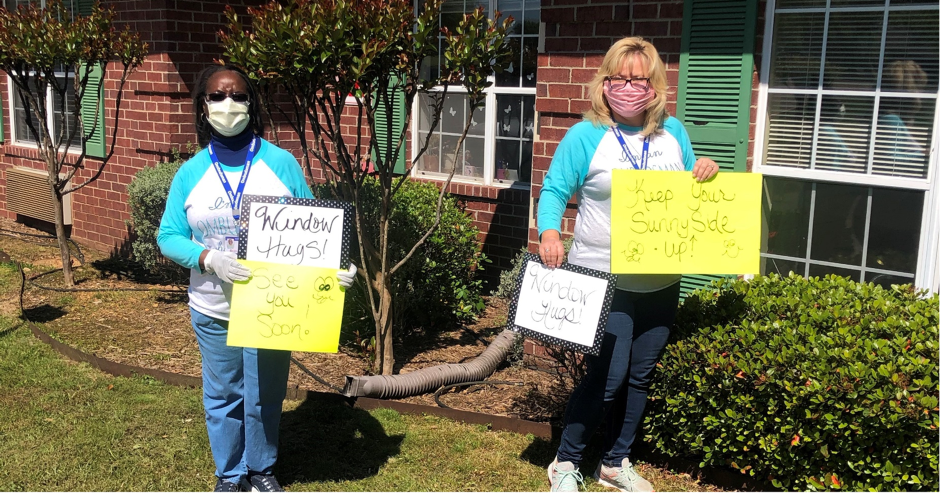 Two women hold signs including "Window Hugs" outside a building